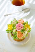 A cupcake with romantic sugar flowers in front of a cup of tea