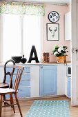 Simple, nostalgic country-house kitchen in pale blue and white with various wooden chairs