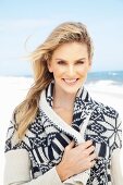 A young blonde woman on a beach wearing a blue-and-white patterned cardigan with a shawl collar