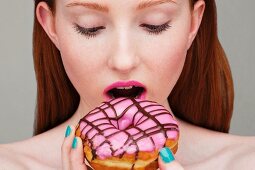 A young woman biting into a pink glazed doughnut, face cropped