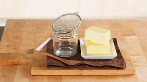 Butterstücke, Einmachglas und Sieb zum Zubereiten von Ghee (Butterschmalz)