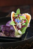 A pita bread filled with a mixed leaf salad, radishes and borage flowers