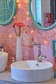 Modern countertop sink with retro tap fitting and oval mirrors with turquoise frames on toile de jouy wallpaper with fairy lights