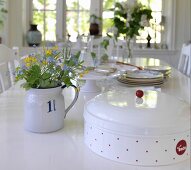 Brotdose und kleiner Blumenstrauss in Vintage Kännchen auf Esstisch