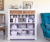Open-fronted crockery cabinet next to swivel armchair with blue upholstery against wood-clad wall
