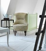Antique easy chair with ornately patterned upholstery in front of stair rail in attic room with white wooden floor