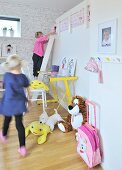 Girls playing in child's bedroom with ladder leading to raised sleeping area, yellow desk and soft toys on floor