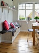 Fur blankets and cushions on bench in dining room with white, wood-clad walls