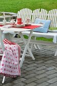 White wooden furniture with colourful scatter cushions and Scandinavian-style crockery on terrace