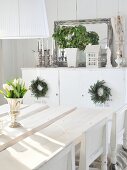 White tulips in silver goblet on rustic white table top; sideboard decorated with candles, plants & mirror in background