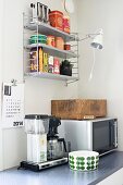 Mikrowelle, Kaffeemaschine und Schüssel auf Küchenarbeitsfläche; Hängeregal mit Vintage Toaster und Klemmleuchte in Retro-Flair Küchenecke