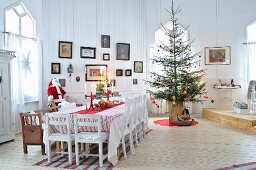 Festively decorated dining table and Christmas tree in interior of Scandinavian wooden house