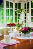 Gedeckter Tisch mit Blumenschale, Kerzen und frischen Erdbeeren