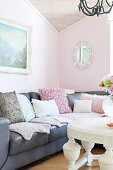 Graue Ledercouch mit verschiedenen Kissen und weisser Couchtisch im Wohnzimmer mit pastellrosa getönter Wand