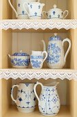 Rustic-style, white crockery with blue painted patterns on shelves with lace trim