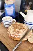 Angeschnittenes Brot mit Messer auf Holzbrett und weiss-blaues Keramikgeschirr