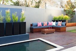 Eingelassenes Wasserbecken in modern gestaltetem Patio, Sitzbank mit Kissen und schwarze Pflanzengefässe mit Euphorbia vor hoher Betonmauer