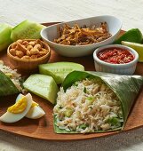 Coconut rice in a banana leaf, eggs, fish, cucumber and a dip (Asia)