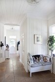 Rustic foyer with white wood cladding, stone floor and bench in foreground with arranged scatter cushions