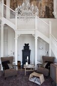 White staircase and balustrade in foyer of country-house villa; 50s armchair and side table on Oriental rug