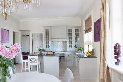 Dining set in open-plan, country-house kitchen with pale grey fronts and bar stools around island counter