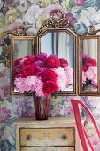 Pfingstrosenstrauss auf Vintage Kommode vor dreiteiligem, verziertem Spiegel und romantischer Blumentapete