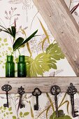 Collection of vintage keys hung from half-timber beams and green glass vases against leaf-patterned wallpaper