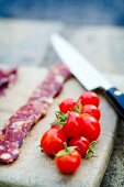 Chorizo slices on a wooden board with cherry tomatoes