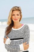 A young blonde woman on a beach wearing a black and white striped knitted jumper