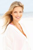 A young blonde woman on a beach wearing a white, transparent blouse