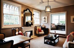 Traditional living room with dining area, dark wood coffee table between sofa and open fireplace and armchair; doorway with steps leading to study in background