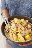 A woman holding a bowl of potato salad with ham, onions and creamy dressing