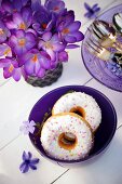 Doughnuts in a purple bowl decorated with purple flowers and a bunch of crocuses