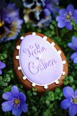 An egg-shaped candle with the words 'Frohe Ostern' surrounded by liverwort floweers