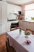 Red and white checked tablecloth on dining table in white, country-house kitchen