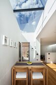 Dining table and chairs made from pale wood below skylight with view of blue sky