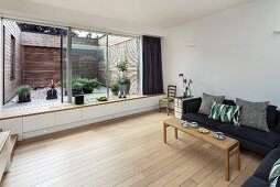 Living room with sofa, wooden floor, glass wall with integrated window seat and view of courtyard