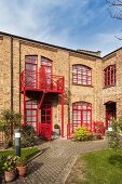 Ehemalige Fabrik als Wohnhaus, rot gestrichene Fensterrahmen und Balkongeländer, davor Innenhof mit eingefassten Beeten und Pflasterwegen