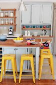 Yellow vintage bar stools at counter in pastel grey Shaker-style kitchen