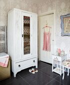 Weiß gestrichener Wäscheschrank, florale Tapete und rosa Vintage Seidenhemdchen auf einem Bügel im Badezimmer