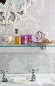 Verschnörkelter Spiegelrahmen, Blumenmuster-Tapete und Glasbord mit romantischen Nippes über Vintage Armatur