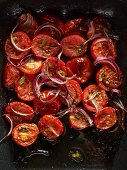 Halved, roasted plum tomatoes with red onion slices and basil leaves in a roasting tin