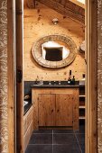 Mirror with oval, wooden frame on rustic wooden wall above washstand with black counter