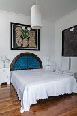 Französisches Bett mit antikem, halbkreisförmigem Kopfteil, darüber Bild an Wand, im Vordergrund Pendelleuchte mit weißem, zylindrischem Stoffschirm