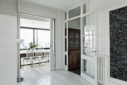 Foyer with white-stained wooden floor and view through open sliding door of dining area with traditional, white chairs