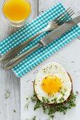 A fried egg on toast with cress and orange juice