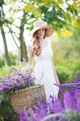 Portrait of beautiful young woman in meadow carrying basket of purple flowers