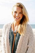 Junge, blonde Frau in beigefarbener Strickjacke am Meer