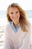 A young blonde woman by the sea wearing a denim shirt and a white woollen jumper