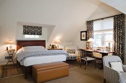 Doppelbett mit gestreifter Bettwäsche und lederbezogene Truhe am Fussende, Schreibtisch am Fenster